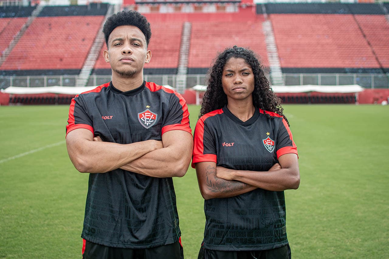 ehety | UAE SPORT STORE Two soccer players with arms crossed on a green pitch, wearing black and red jerseys, in a stadium.