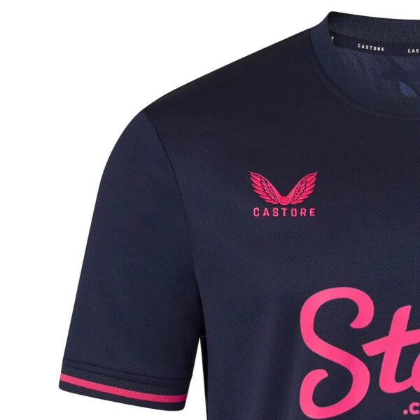 Close-up of a navy Castore sports jersey showing a pink winged logo on the chest and part of large pink script text.