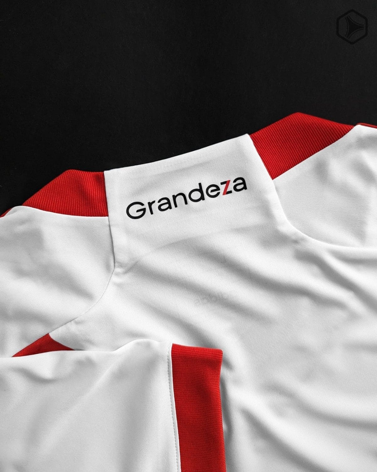 Close-up of a white jersey with red trim and the word Grandeza printed on it.