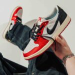 Close-up of a hand holding a red, white, and black Nike Air Jordan 1 sneaker against a light background