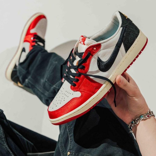 Close-up of a hand holding a red, white, and black Nike Air Jordan 1 sneaker against a light background