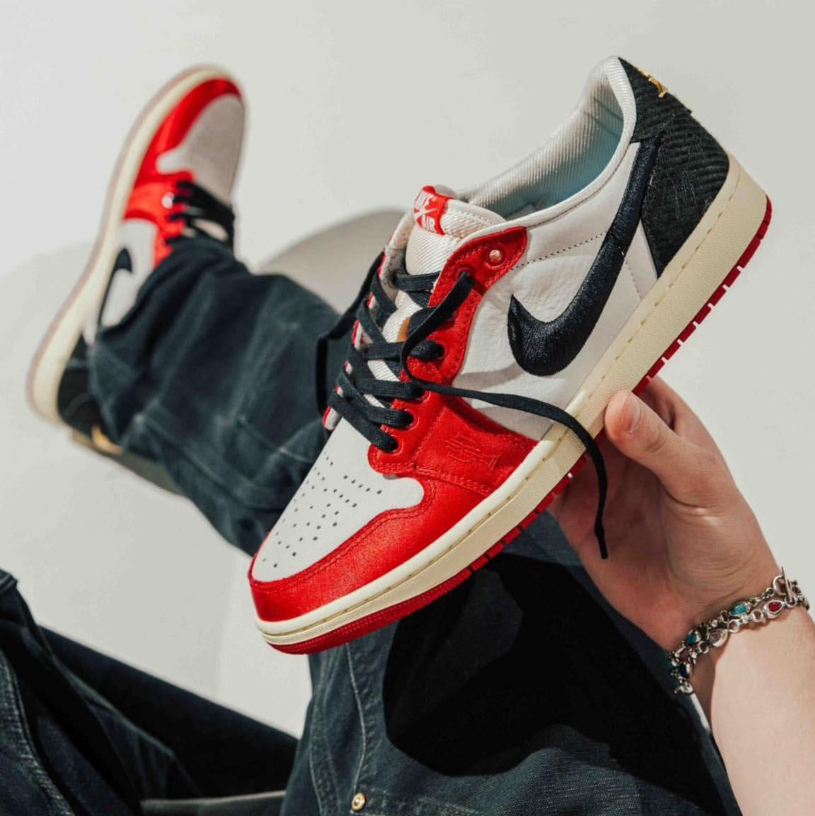 f00ec8b1-59f1-478b-a347-a9e69fe598ef Close-up of a hand holding a red, white, and black Nike Air Jordan 1 sneaker against a light background