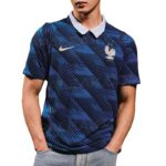 Male model wearing a navy blue patterned polo shirt with a white collar, featuring a Nike swoosh and the French Football Federation crest on the chest, hands in pockets.
