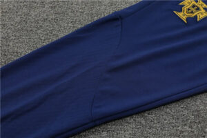 Blue sleeve of a garment with a partial gold badge embroidery at the shoulder area on gray carpeted background.