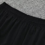 Close-up of a black elastic waistband on a pair of pants laid on a gray carpet.