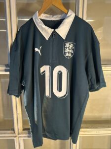 Dark teal England football jersey on a hanger with a white collar, featuring a left chest crest and large number 10 on the front.