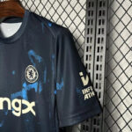 Dark blue Chelsea FC soccer jersey with light blue splashes, hanging on a hanger against a metal rack.