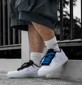 Person wearing white sneakers with blue laces stepping onto a curb, socks visible, urban railing in background
