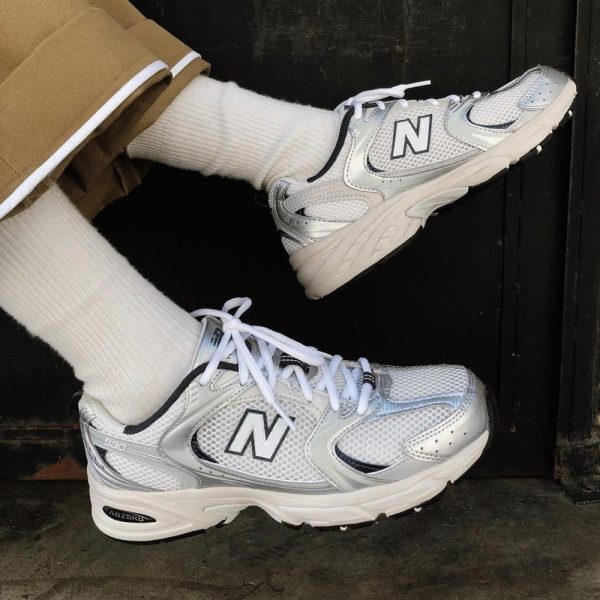 Person wearing white socks and silver-white New Balance sneakers resting on a dark doorstep or threshold.