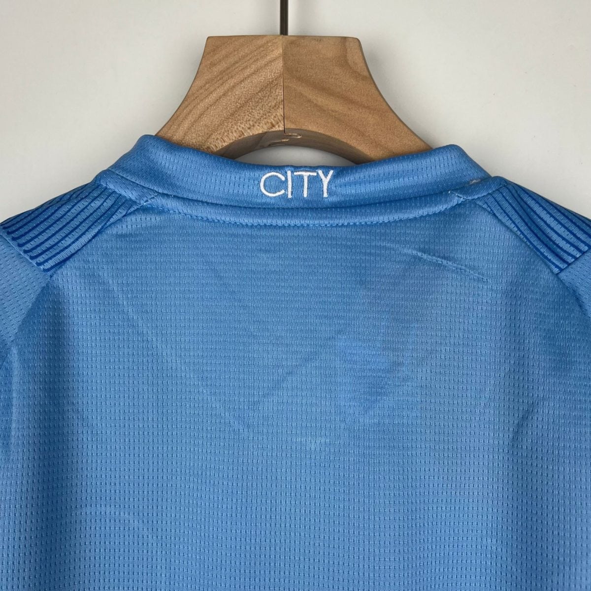 Blue polo shirt on a wooden hanger, back of the neck showing white 'CITY' embroidery.