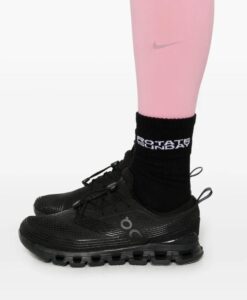 f239e521-268d-4988-8adb-0acdac7de637 | UAE SPORT STORE Close-up of a black running shoe with a thick sole, worn with a black crew sock featuring white lettering on a pink leg.