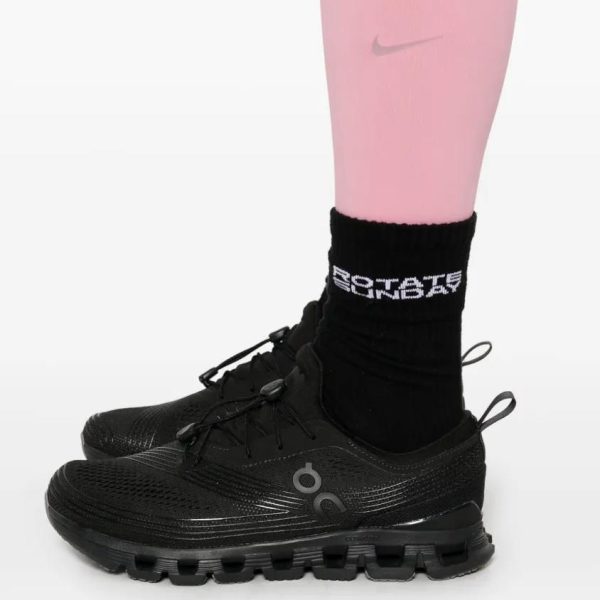 Close-up of a black running shoe with a thick sole, worn with a black crew sock featuring white lettering on a pink leg.