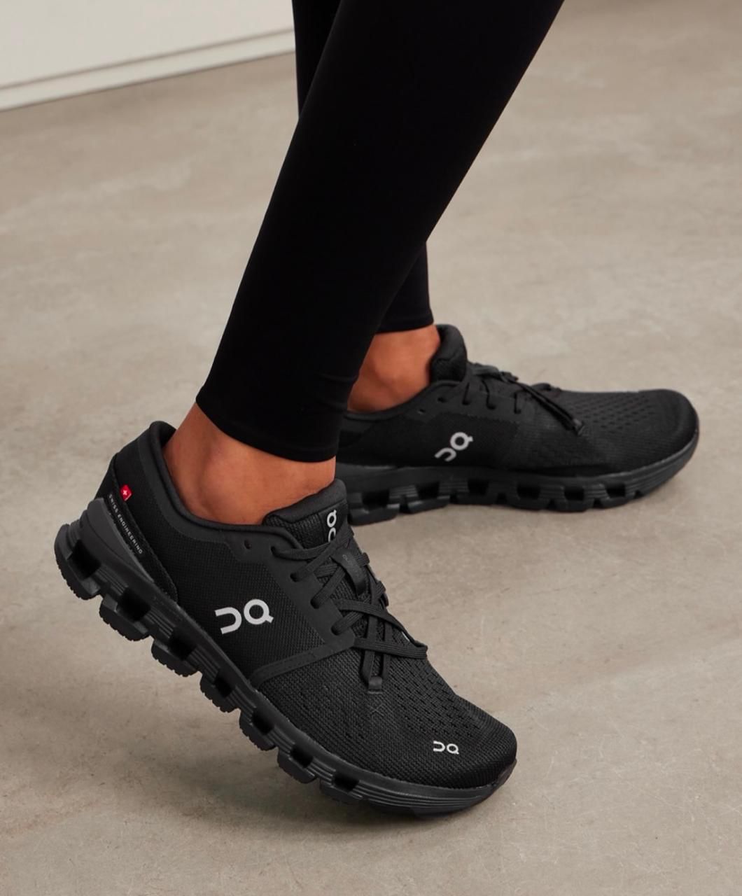 f2456ba2-2709-4361-8435-d5d5ea96bafe | UAE SPORT STORE Person wearing black athletic shoes and black leggings, standing on a light floor, showing the On logo on the sides.