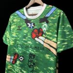 Green sports jersey on a hanger with a cartoon hand graphic, Werder Bremen crest, and Hummel logo; handwritten '1.FC BLAUMEIER' text visible.