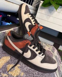 Pair of black, cream, and rust-colored sneakers with a white Nike swoosh resting on a purple rug.