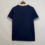 Back view of a navy polo shirt on a wooden hanger, white collar showing at the neck and white-and-navy striped cuffs visible on the sleeves.