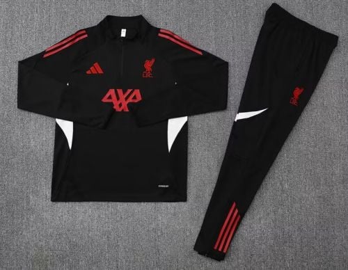 Black Liverpool FC training tracksuit laid flat: zip-up jacket and matching pants with red accents on a gray surface (logo and stripes visible).