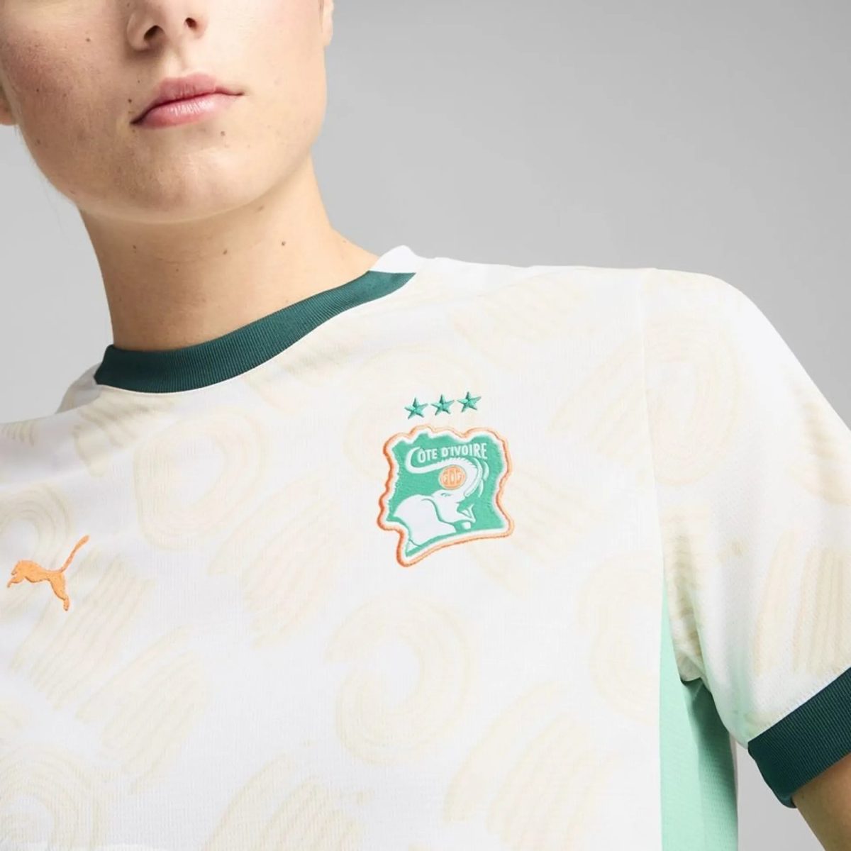 Partial view of a person’s lower face and neck wearing a white jersey with a green collar and a Côte d'Ivoire crest on the chest.