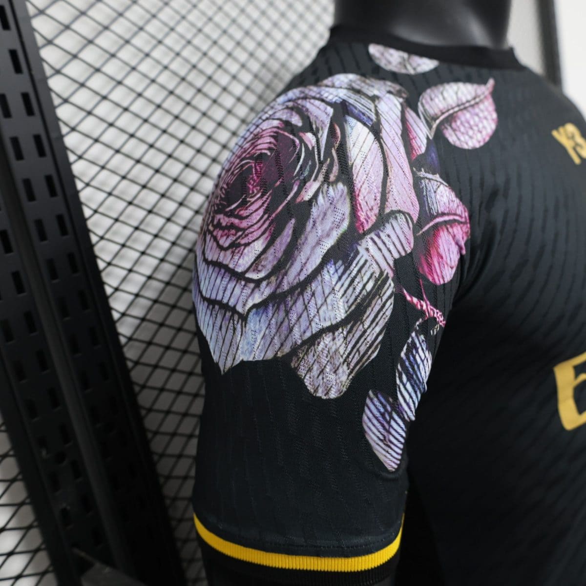 Close-up of black athletic fabric with a purple-pink floral pattern and yellow trim on the sleeve, with a mesh grid background behind it.