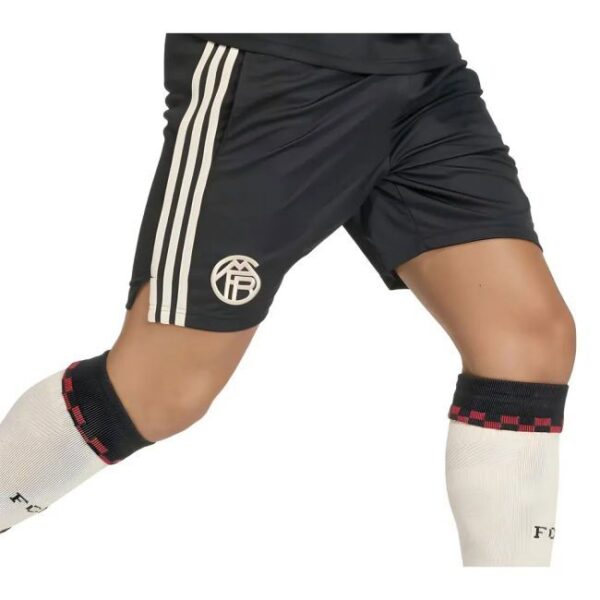 Close-up of a soccer player’s legs in black shorts with white stripes and a circular logo, wearing white socks with black and red trim.