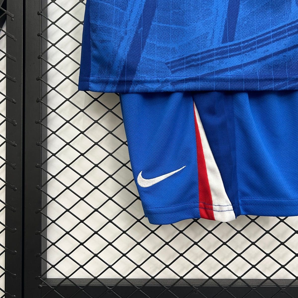 Blue athletic jersey draped over a black chain-link fence, with a white Nike swoosh visible at the bottom corner.