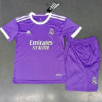 Purple Real Madrid football jersey with Emirates Fly Better sponsor, Adidas logo, team crest, white trim, and a matching purple shorts with Real Madrid crest on the leg; tag attached.