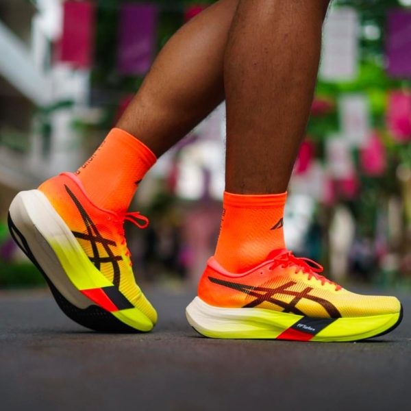Close-up of bright neon orange and yellow running shoes in mid-stride on a city street outside.