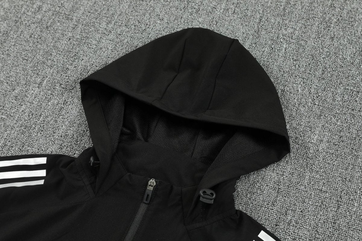 Black hooded jacket laid flat on a gray carpet, zipper visible along the front, white striped sleeve detail partially shown.