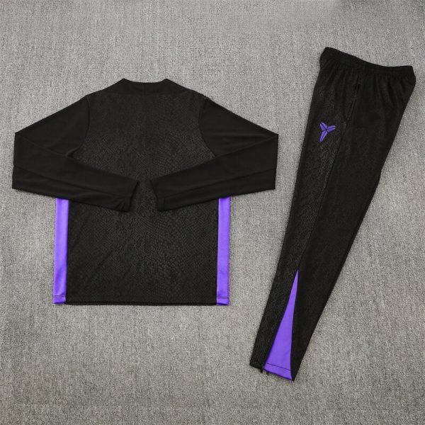 Matching black athletic outfit: long-sleeve top with purple side panels and subtle texture, placed beside black leggings with purple accents and logo on a gray carpet.