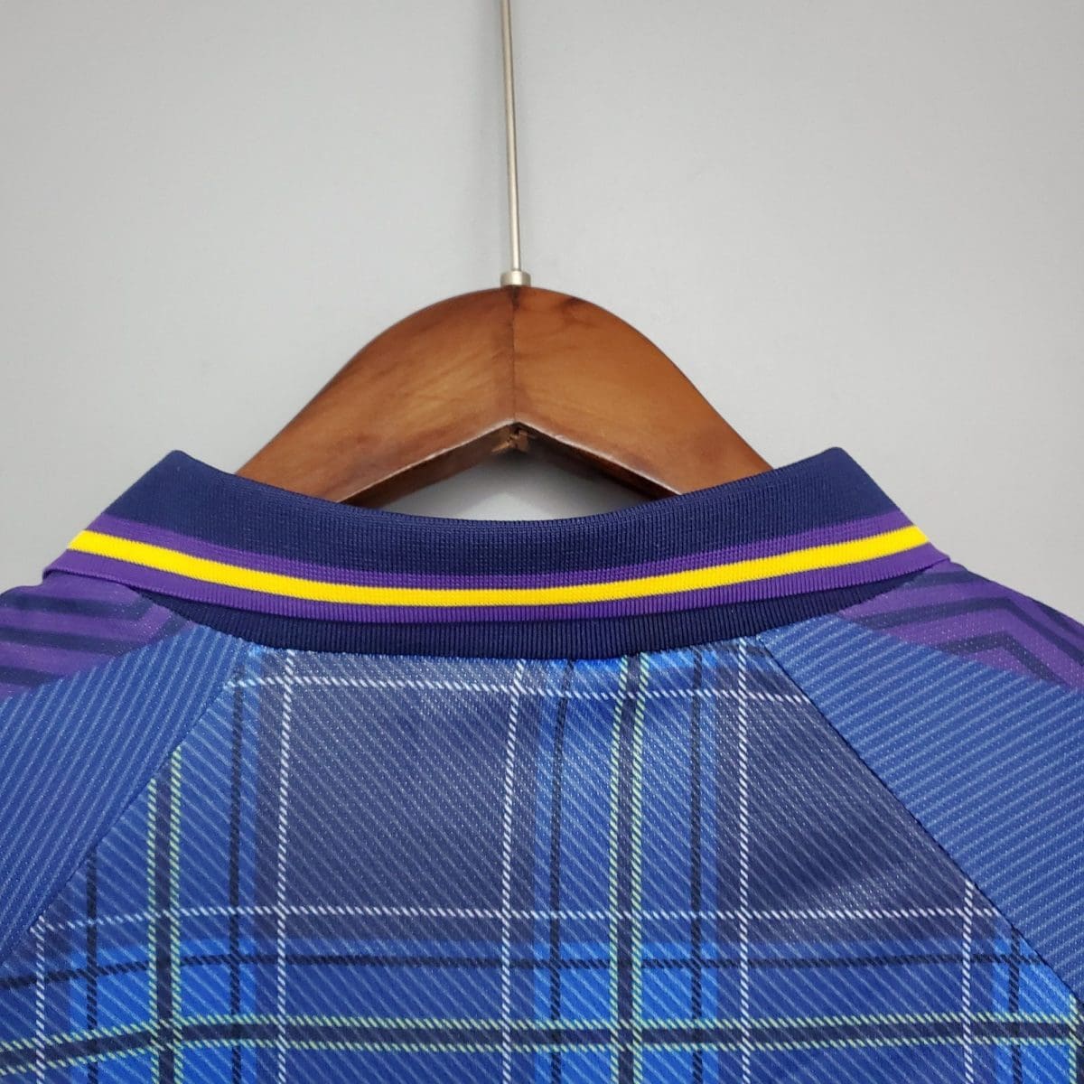 Blue plaid shirt on a wooden hanger, close-up of the collar against a light wall.