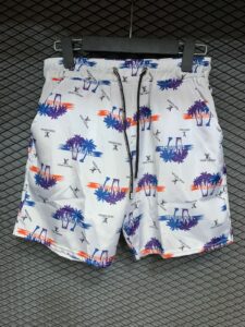 White Louis Vuitton swim shorts with blue, purple palm trees and orange sunset accents on a white background, hanging on a rack
