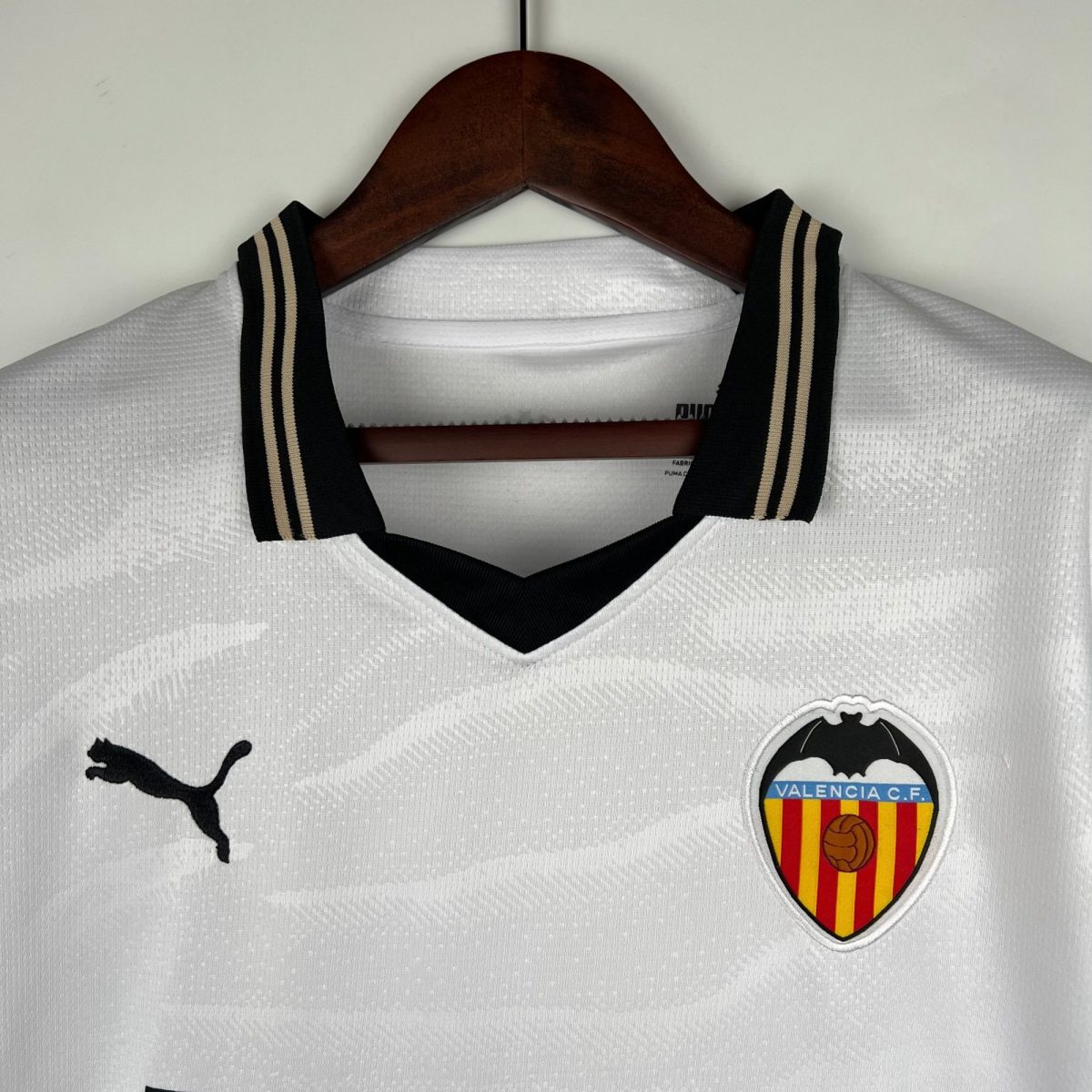 White textured polo shirt on a wooden hanger with black-and-beige striped collar, featuring a Puma logo on the left and a Valencia CF crest on the right