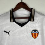 White textured polo shirt on a wooden hanger with black-and-beige striped collar, featuring a Puma logo on the left and a Valencia CF crest on the right