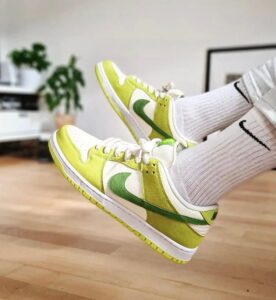 Lime green and white Nike sneakers worn with white socks, indoors on a wooden floor.