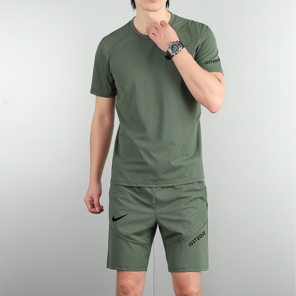 Partial body of a man in olive-green athletic wear against a gray backdrop, with visible Nike swoosh on shorts and 'JUST DO IT' text on the leg.