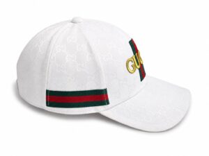 White Gucci baseball cap with an embossed GG pattern, green-red stripe on the back, and gold Gucci lettering on the front.