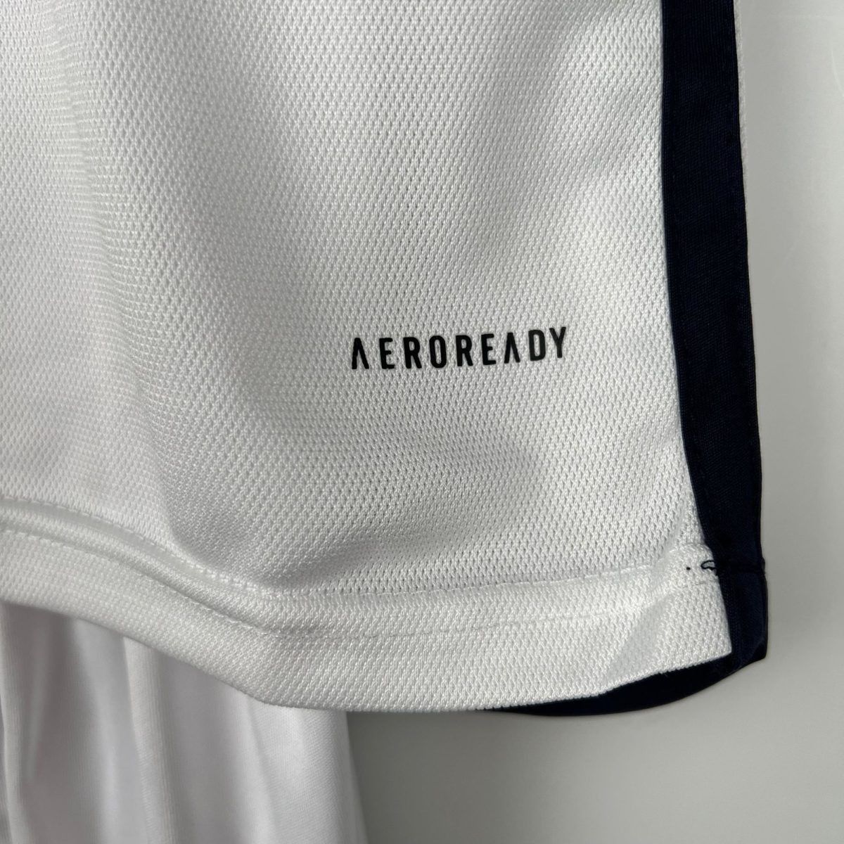 Close-up of white textured fabric with a dark vertical stripe and the word 'AEROREADY' partially visible.