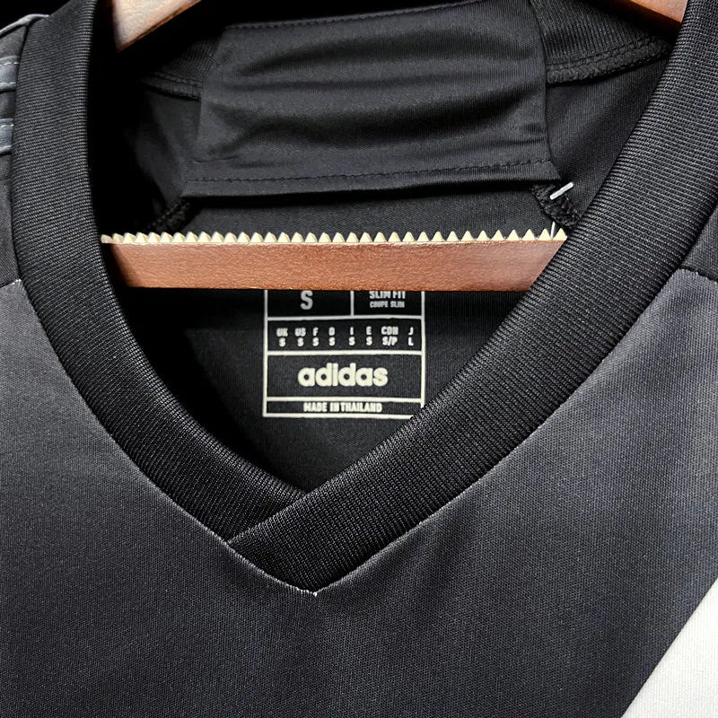 f5ebbf895f66123e_6c070ffa-feef-448a-8d0b-85dc6b4f7089 | UAE SPORT STORE Close-up of a black Adidas sports top on a hanger, showing the V-neck collar and Adidas label (Made in Thailand, size S).