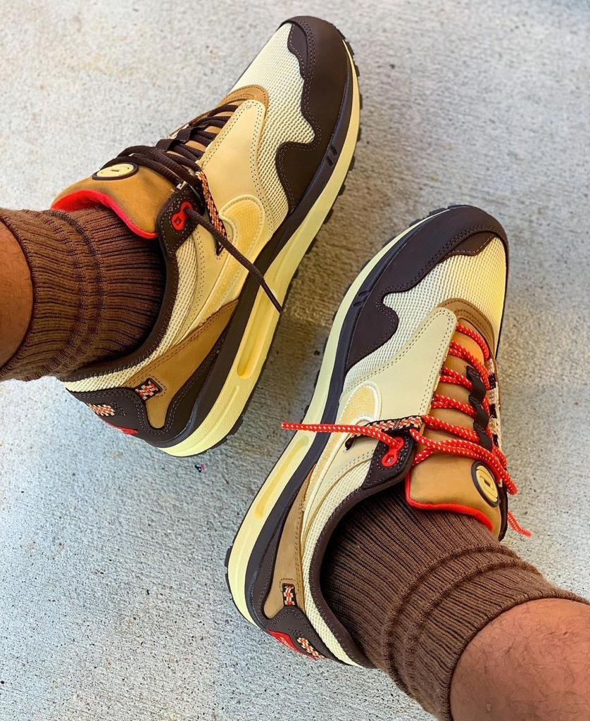 f5f8c5cf-0220-451c-81a8-c15c7031fb43_40a0b70d-abaf-41a2-8ea8-d1ad81a9e849 | UAE SPORT STORE Pair of beige and brown sneakers with red laces on a concrete floor, worn with brown socks.