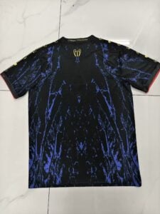 Black football jersey with a blue marbled pattern, small gold trophy emblem at the upper back, and 'COMMA FOOTBALL' on the collar with red-trimmed sleeves.