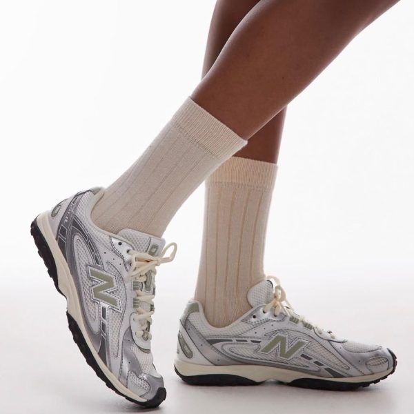 Lower legs wearing cream socks and gray-white New Balance sneakers on a white background, side view.