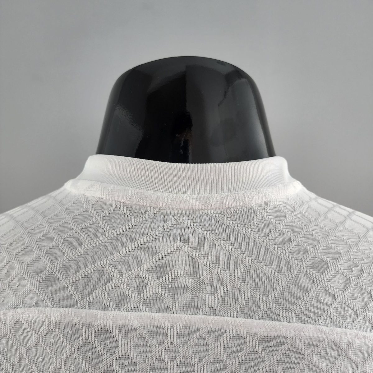 Back view of a glossy black mannequin head wearing a white knit collar against a gray background
