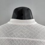 Back view of a glossy black mannequin head wearing a white knit collar against a gray background