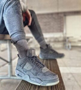 Close-up of a gray sneaker resting on a wooden bench, with a ribbed gray sock visible and denim pant leg folded up nearby.