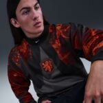 Person wearing a black and red athletic top with a lion crest, posing against a gray backdrop.