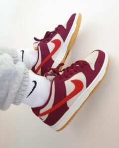 f887441e-d63b-42db-8168-0eb9d40a2229_fd060b35-c95c-4568-9258-e128bb46af1c | UAE SPORT STORE Pair of maroon, white, and orange Nike sneakers with gum soles resting on a light floor, plus white socks showing the Nike logo.