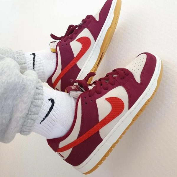 Pair of maroon, white, and orange Nike sneakers with gum soles resting on a light floor, plus white socks showing the Nike logo.