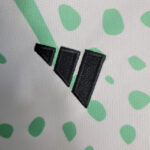 Close-up of a black stitched logo with three angled shapes on white textured fabric with mint green dots.