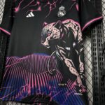 Black Real Madrid soccer jersey with a bold pink panther graphic, pink lightning accents, and a blue‑purple striped hem; Adidas logo visible and AEROREADY branding near the bottom hem
