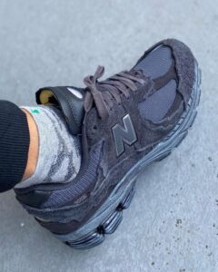 Close-up of a dark gray New Balance 2002R sneaker on a gray camo sock, resting on concrete surface.